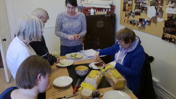 Group of four people with learning disabilities and trainer working with sliced bread and fruit